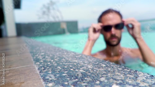 the young man takes the sunglasses lying next to the swimming pool puts them on and swims forward