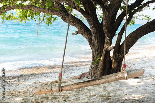 Empty wooden swing on an exotic beach - Ko Kham island, Thailand, Andaman Sea. Wodden swing tied with ropes to a big tree with sea in the background.