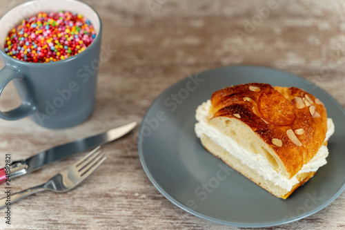 A piece of king's cake made by hand in the oven, on a cozy wooden base, and a cup with colorful chocolate topping.