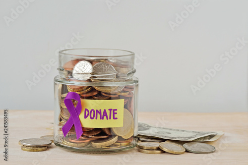 Money jar full of coins with violet ribbon and Donate label - Concept of Alzheimer, Pancreatic cancer, Epilepsy , Hodgkin's Lymphoma charity and research fund photo