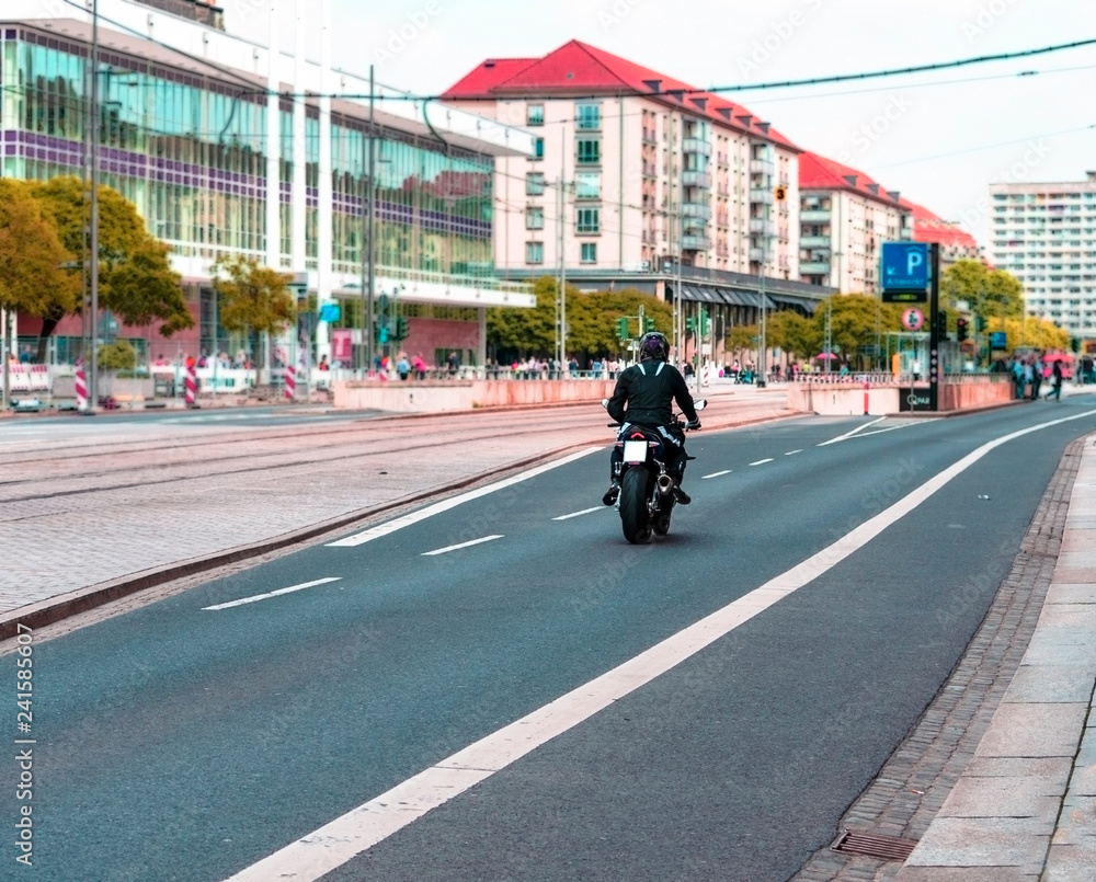 Motorcycle driver, motorcyclist, moves on the road of the city. Blurred background, view from the back.