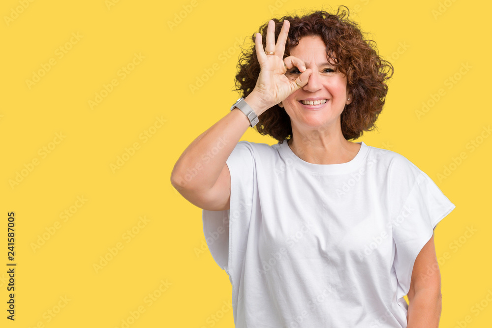 Beautiful middle ager senior woman wearing white t-shirt over isolated background doing ok gesture with hand smiling, eye looking through fingers with happy face. Beautiful middle ager senior woman wearing white t-shirt over isolated background doing ok gesture with hand smiling, eye looking through fingers with happy face.