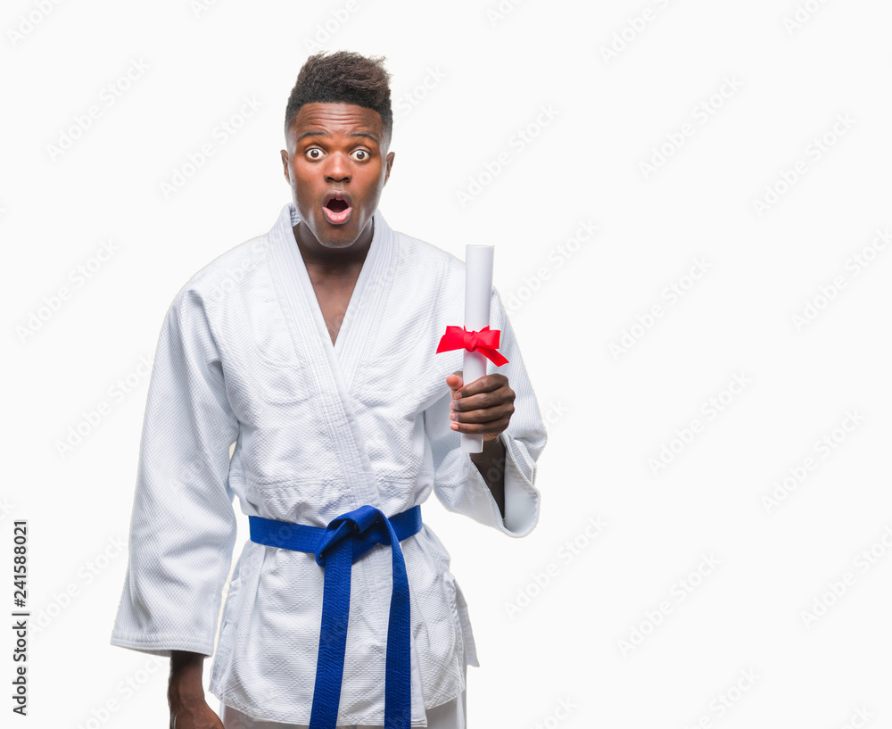 Young african american man over isolated background wearing kimono holding degree scared in shock with a surprise face, afraid and excited with fear expression Young african american man over isolated background wearing kimono holding degree scared in shock with a surprise face, afraid and excited with fear expression