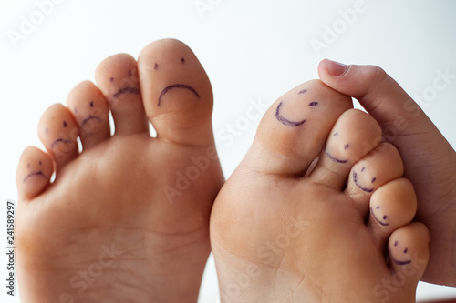 Female toes with painted smileys and children's hands. Foot care concept, pedicure.