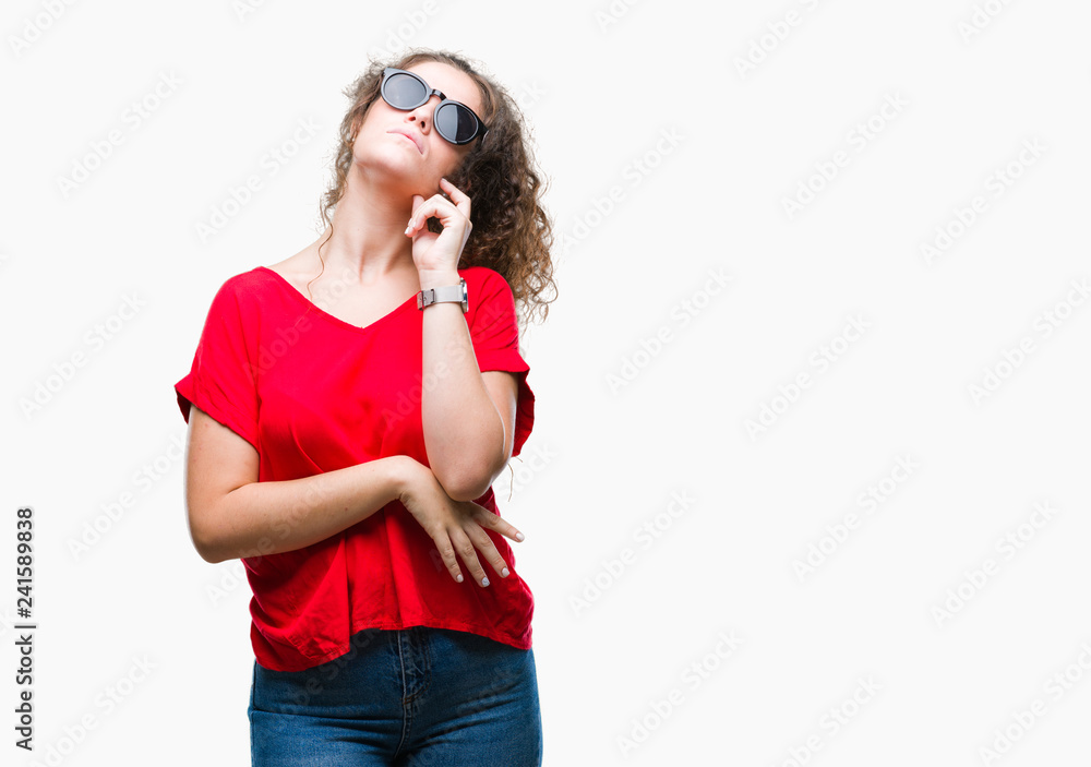 Beautiful brunette curly hair young girl wearing sunglasses over isolated background with hand on chin thinking about question, pensive expression. Smiling with thoughtful face. Doubt concept. Beautiful brunette curly hair young girl wearing sunglasses over isolated background with hand on chin thinking about question, pensive expression. Smiling with thoughtful face. Doubt concept.