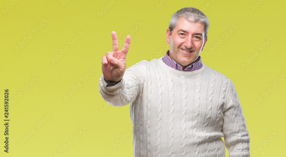 Fototapeta premium Handsome senior man wearing winter sweater over isolated background smiling with happy face winking at the camera doing victory sign. Number two.