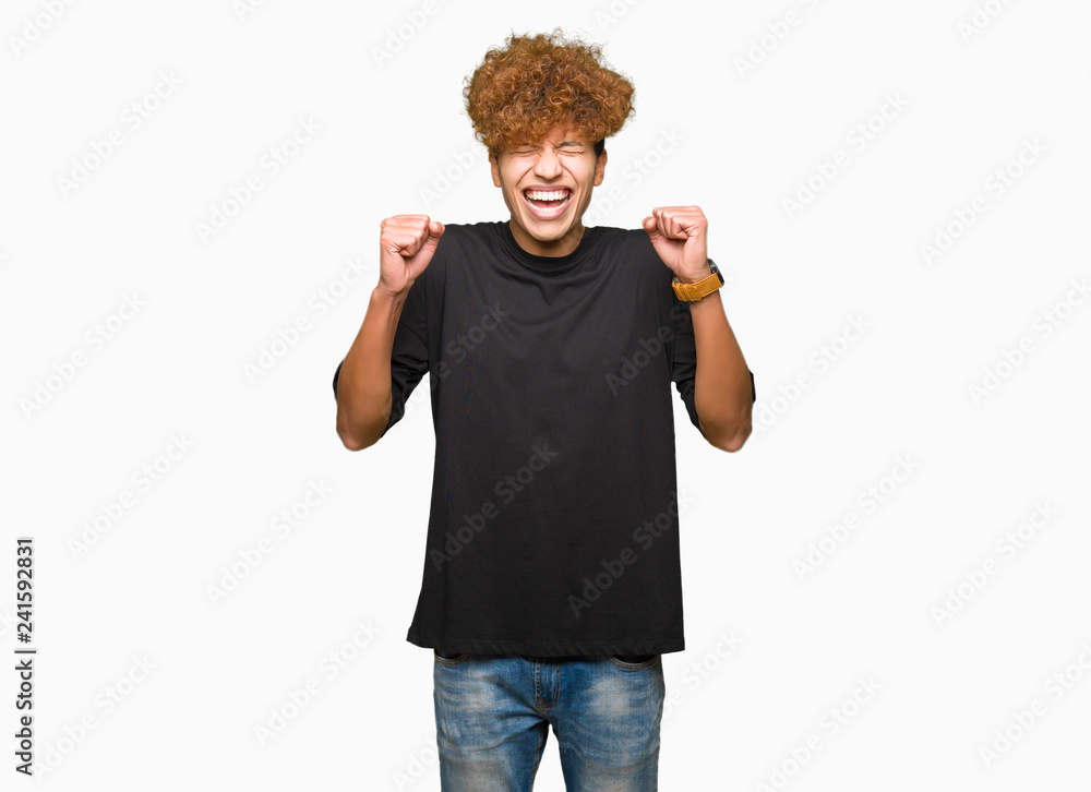Young handsome man with afro hair wearing black t-shirt excited for success with arms raised celebrating victory smiling. Winner concept. Young handsome man with afro hair wearing black t-shirt excited for success with arms raised celebrating victory smiling. Winner concept.