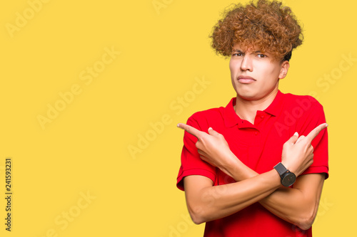 Young handsome man with afro hair wearing red t-shirt Pointing to both sides with fingers, different direction disagree
