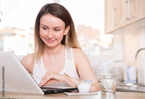 Smiling woman is working with laptop sitting at the table