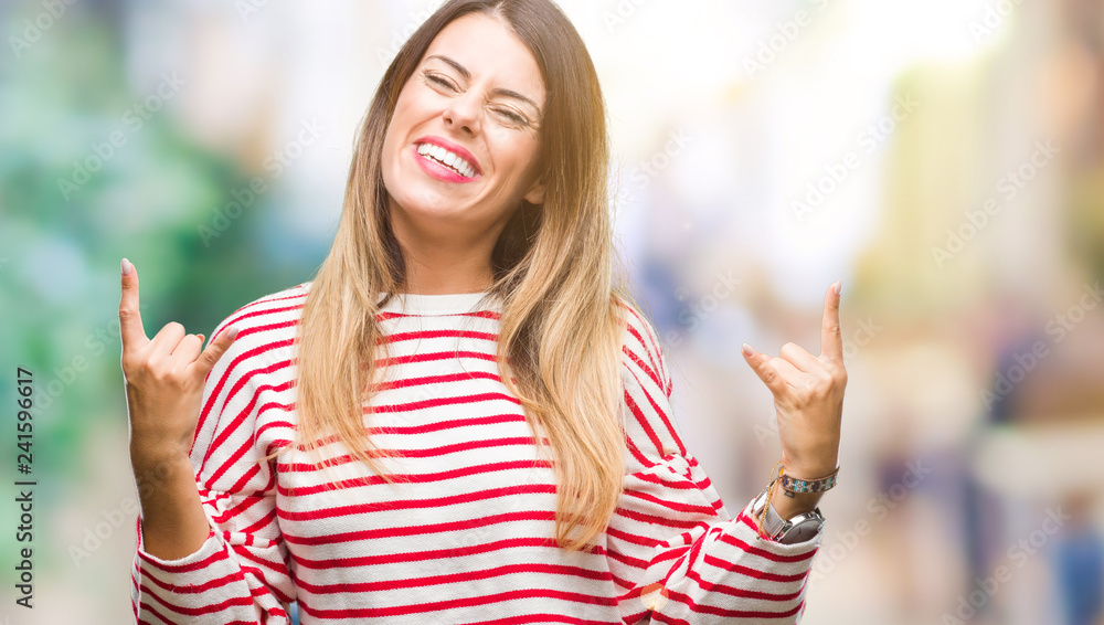 Young beautiful woman casual stripes winter sweater over isolated background shouting with crazy expression doing rock symbol with hands up. Music star. Heavy concept.