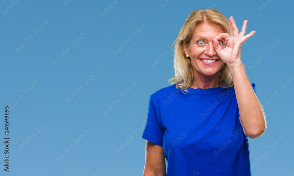 Fototapeta premium Middle age blonde woman over isolated background doing ok gesture with hand smiling, eye looking through fingers with happy face.