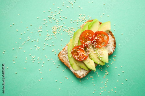 Flat lay of delicious toasts with sliced avocado, tomatoes and sesamum seeds on turqouise background with copyspace. Healthy food concept. photo