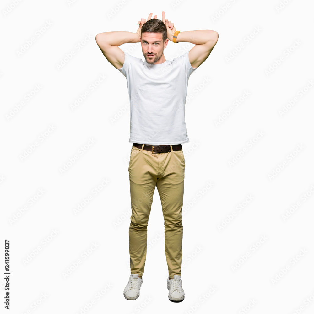 Handsome man wearing casual white t-shirt Posing funny and crazy with fingers on head as bunny ears, smiling cheerful Handsome man wearing casual white t-shirt Posing funny and crazy with fingers on head as bunny ears, smiling cheerful