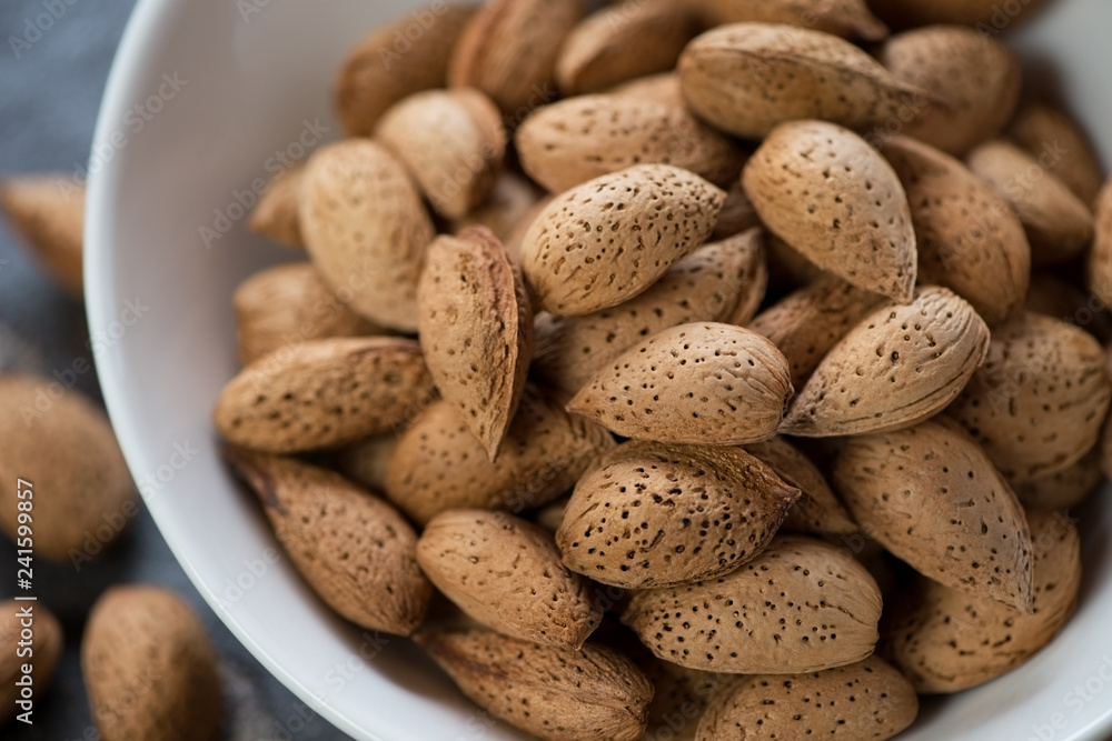 Close-up of unpeeled almond nuts in a white bowl, selective focus, studio shot Close-up of unpeeled almond nuts in a white bowl, selective focus, studio shot