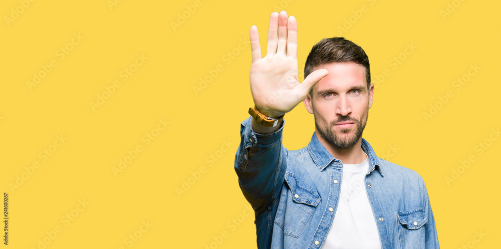 Handsome man with blue eyes and beard wearing denim jacket doing stop sing with palm of the hand. Warning expression with negative and serious gesture on the face.