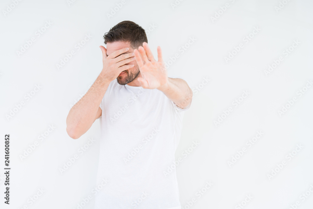 Young handsome man wearing casual white t-shirt over isolated background covering eyes with hands and doing stop gesture with sad and fear expression. Embarrassed and negative concept. Young handsome man wearing casual white t-shirt over isolated background covering eyes with hands and doing stop gesture with sad and fear expression. Embarrassed and negative concept.