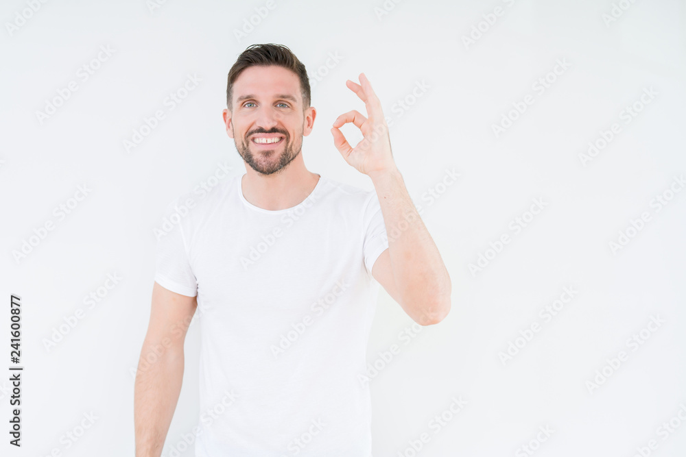 Young handsome man wearing casual white t-shirt over isolated background smiling positive doing ok sign with hand and fingers. Successful expression. Young handsome man wearing casual white t-shirt over isolated background smiling positive doing ok sign with hand and fingers. Successful expression.