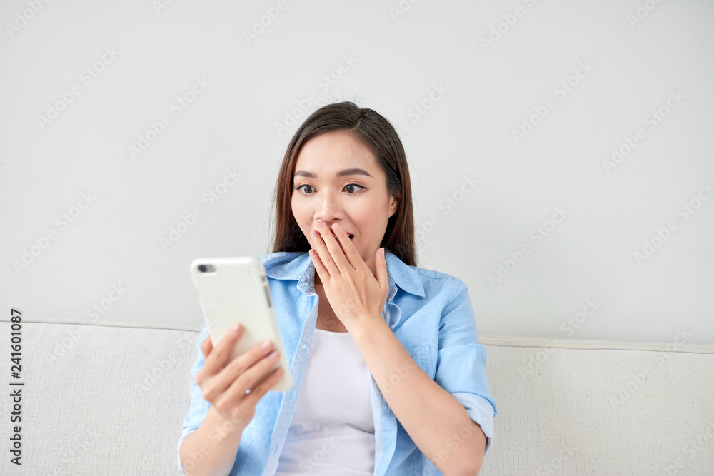 Excited woman reading text on a phone lying on a couch in the living room at home Excited woman reading text on a phone lying on a couch in the living room at home