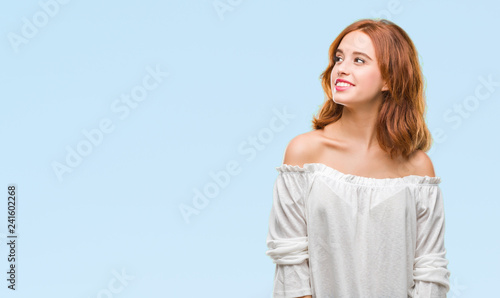 Young beautiful woman over isolated background looking away to side with smile on face, natural expression. Laughing confident.