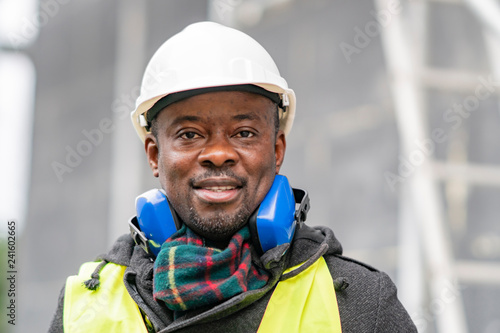 Portrait of an African American engineer wearing safety equipment (headphones, helmet and jacket) looking at the camera