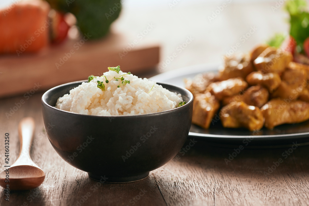 White rice with curry and chicken in black plate on wooden table White rice with curry and chicken in black plate on wooden table