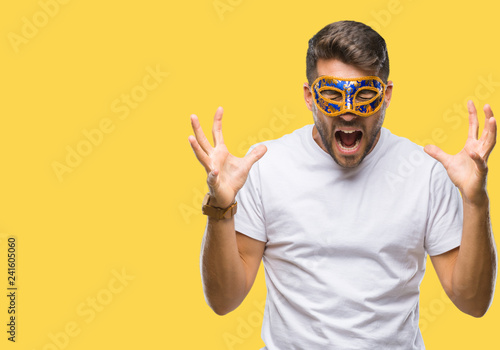 Young handsome man wearing carnival mask over isolated background celebrating mad and crazy for success with arms raised and closed eyes screaming excited. Winner concept © Krakenimages.com