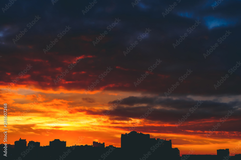 Cityscape with wonderful varicolored vivid fiery dawn. Amazing dramatic multicolored cloudy sky. Dark silhouettes of city buildings. Atmospheric background of sunrise in overcast weather. Copy space.