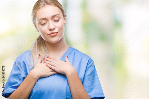 Young blonde surgeon doctor woman wearing medical uniform over isolated background smiling with hands on chest with closed eyes and grateful gesture on face. Health concept.