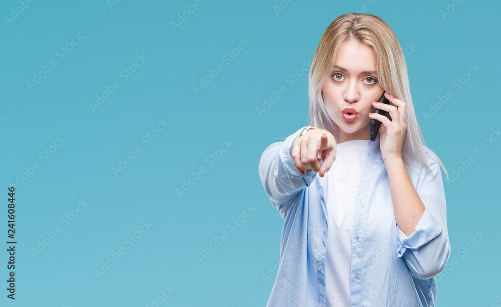 Young blonde woman talking using smarpthone over isolated background pointing with finger to the camera and to you, hand sign, positive and confident gesture from the front Young blonde woman talking using smarpthone over isolated background pointing with finger to the camera and to you, hand sign, positive and confident gesture from the front