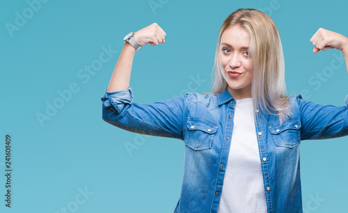 Young blonde woman over isolated background showing arms muscles smiling proud. Fitness concept.