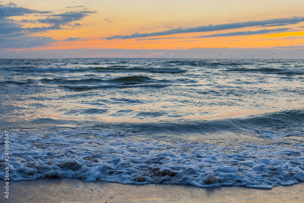 Low waves on Baltic sea at sunset. Cosy flat sandy beach.