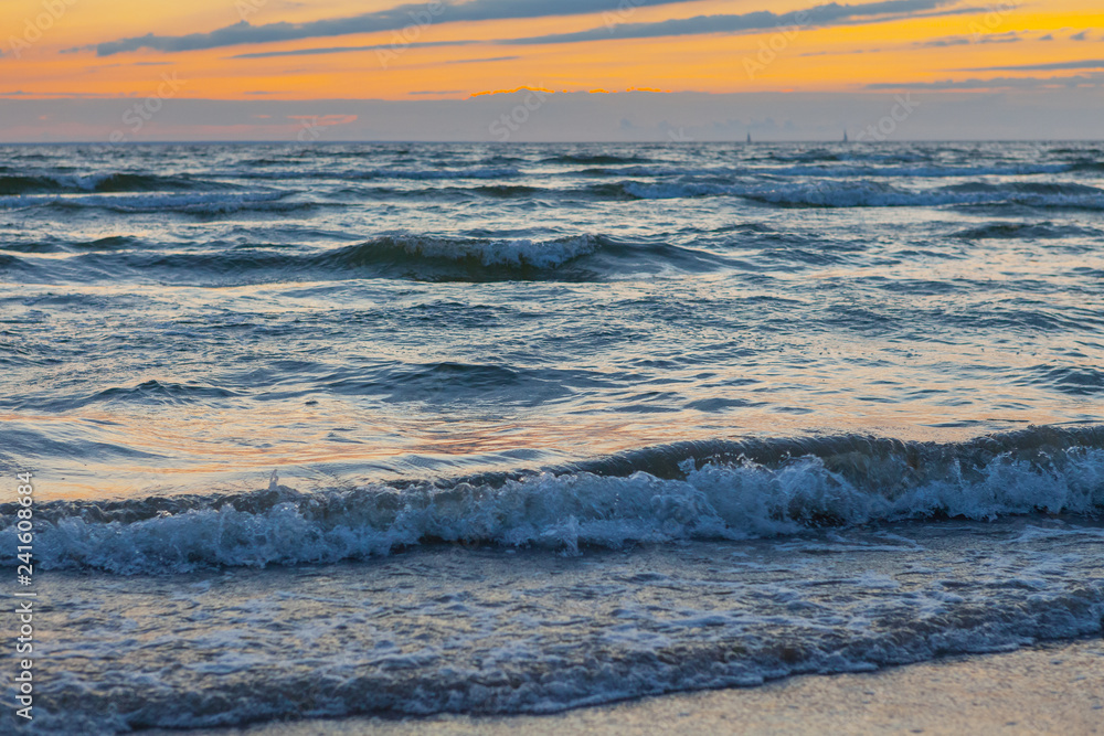 Low waves on Baltic sea at sunset. Cosy flat sandy beach.