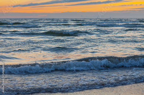 Low waves on Baltic sea at sunset. Cosy flat sandy beach.