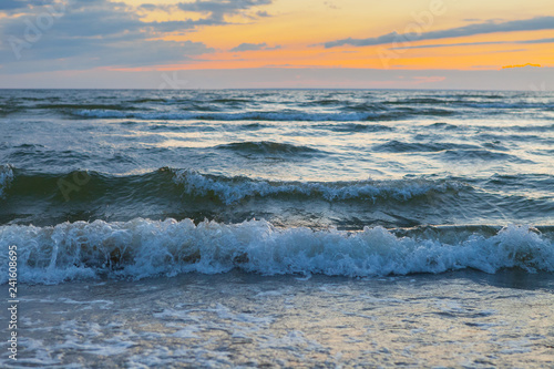 Low waves on Baltic sea at sunset. Cosy flat sandy beach.