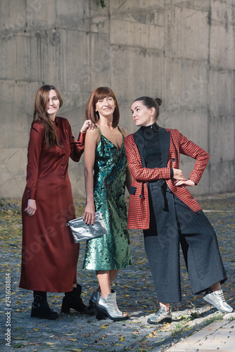 Street style Fashion portrait three charming women. Brown and green dress, Black, tile red jacket, silver shoes. Summer Spring Fall collection beautiful look. Togetherness, friendship, party concept