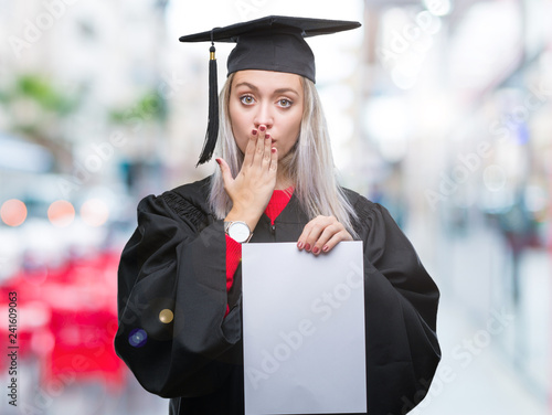 Young blonde woman wearing graduate uniform holding degree over isolated background cover mouth with hand shocked with shame for mistake, expression of fear, scared in silence, secret concept