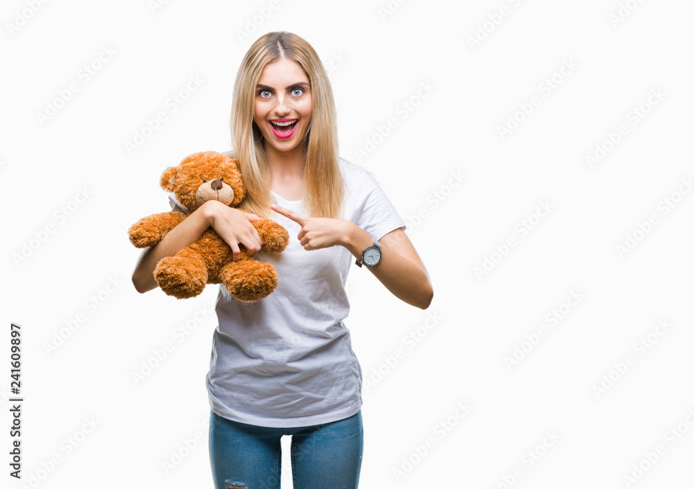 Young beautiful blonde woman holding teddy bear over isolated background very happy pointing with hand and finger Young beautiful blonde woman holding teddy bear over isolated background very happy pointing with hand and finger