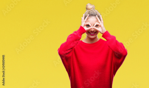 Young beautiful blonde woman wearing red sweater and glasses over isolated background doing ok gesture like binoculars sticking tongue out, eyes looking through fingers. Crazy expression.