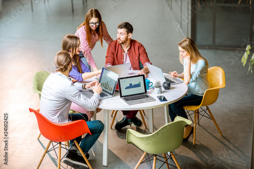 Team of a young coworkers dressed casually working together with laptops sitting at the round table in the office photo