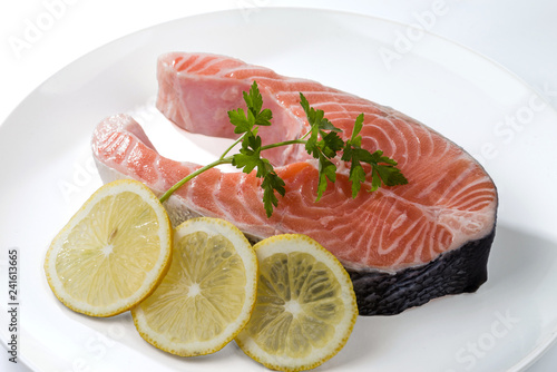 Salmon steak with a sprig of parsley and three lemon slices on a white plate.