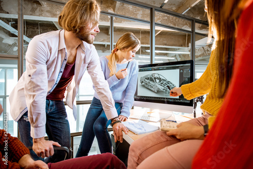 Group of young creative coworkers designing a car model at the working place with computers in the modern office interior photo