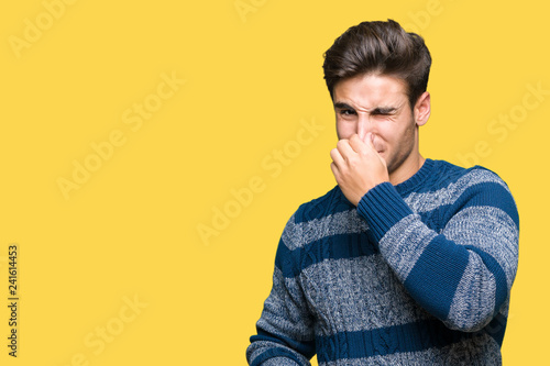 Young handsome man over isolated background smelling something stinky and disgusting, intolerable smell, holding breath with fingers on nose. Bad smells concept. © Krakenimages.com