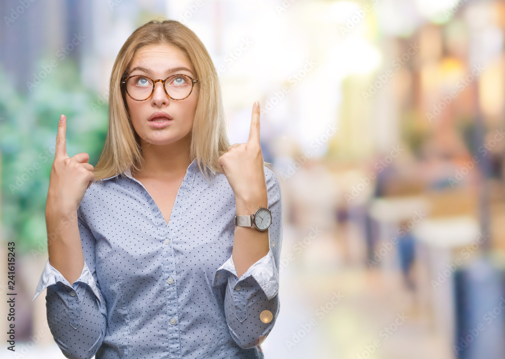 Young caucasian business woman wearing glasses over isolated background amazed and surprised looking up and pointing with fingers and raised arms. Young caucasian business woman wearing glasses over isolated background amazed and surprised looking up and pointing with fingers and raised arms.