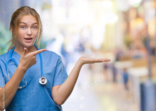 Young caucasian doctor woman wearing surgeon uniform over isolated background amazed and smiling to the camera while presenting with hand and pointing with finger.