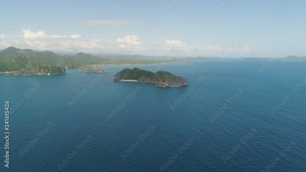 Aerial view of Groups islands with sand beach and turquoise water in blue lagoon among coral reefs, Caramoan Islands, Philippines. Mountains covered with tropical forest.