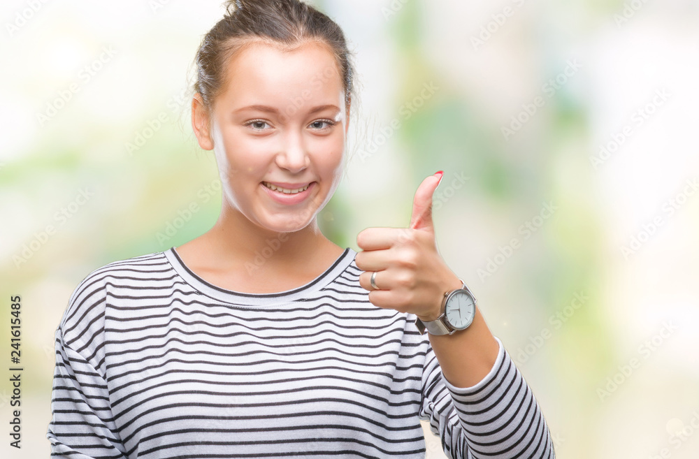 Young beautiful caucasian woman over isolated background doing happy thumbs up gesture with hand. Approving expression looking at the camera with showing success. Young beautiful caucasian woman over isolated background doing happy thumbs up gesture with hand. Approving expression looking at the camera with showing success.