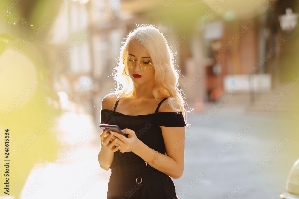 Obraz premium emotional blond girl in sunglasses with phone in summer sunshine