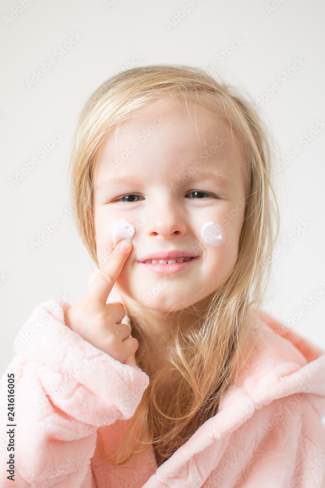 Little young girl applying moisturizing cream on her face. Skin care and beauty concept Little young girl applying moisturizing cream on her face. Skin care and beauty concept