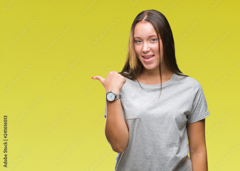 Young caucasian beautiful woman over isolated background smiling with happy face looking and pointing to the side with thumb up. Young caucasian beautiful woman over isolated background smiling with happy face looking and pointing to the side with thumb up.