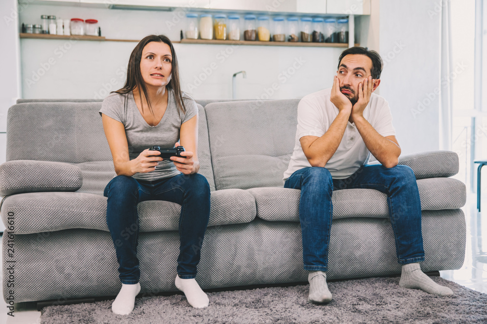 The wife plays the game while the man just sits The wife plays the game while the man just sits